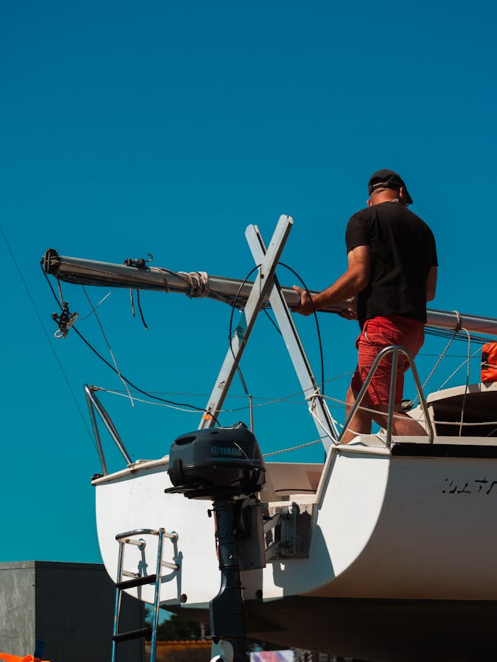 services-01 Man on a sailboat setting up for a day on the water, under clear blue skies.