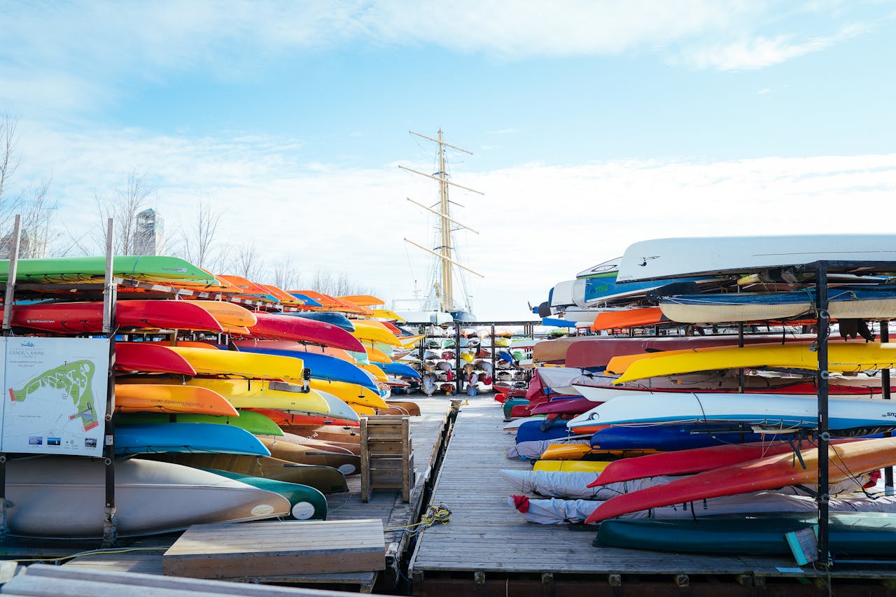 about-me-img Vibrant canoes and kayaks neatly stacked on a dock under a blue sky, perfect for recreational activities.