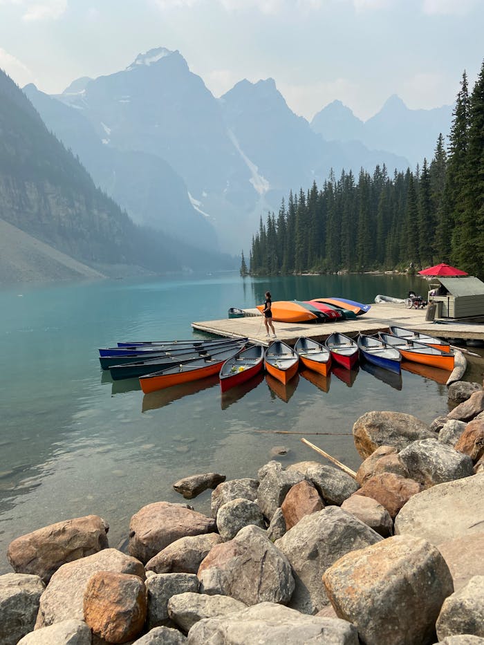 service-02 Woman standing on pier with colorful canoes in beautiful Moraine Lake scenery.