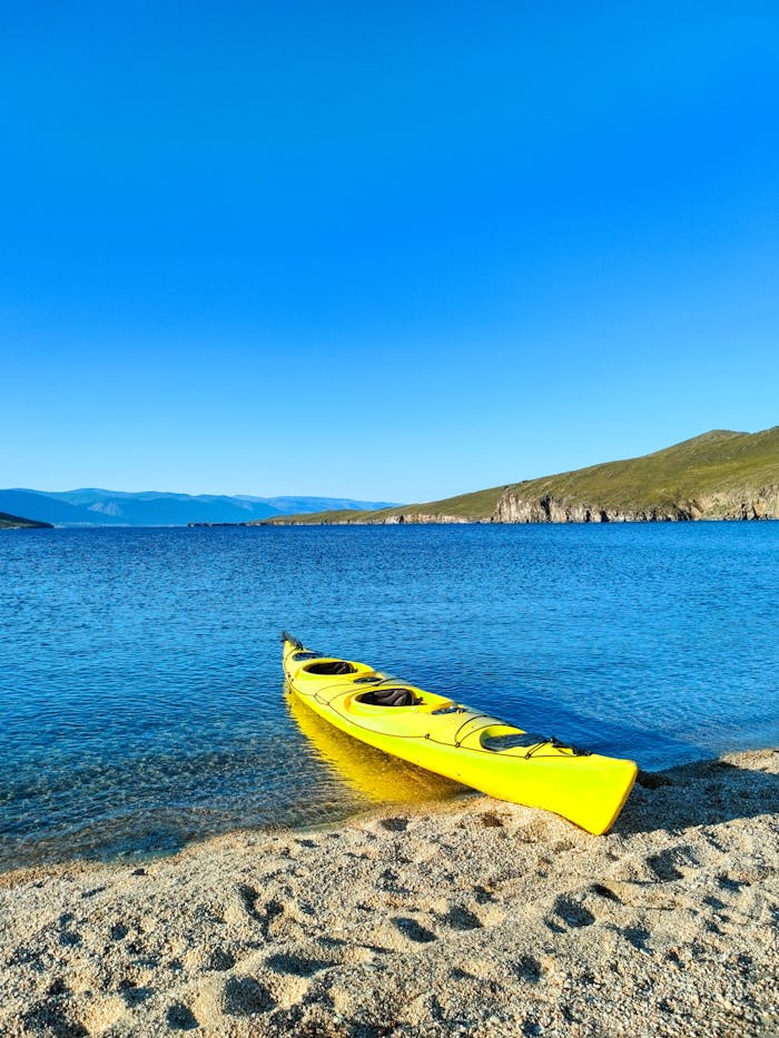 services-img A bright yellow kayak rests on the sandy shores of Lake Baikal under clear blue skies.